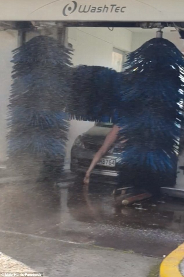 Naked man lying on his vehicle while inside of a drive-through car wash