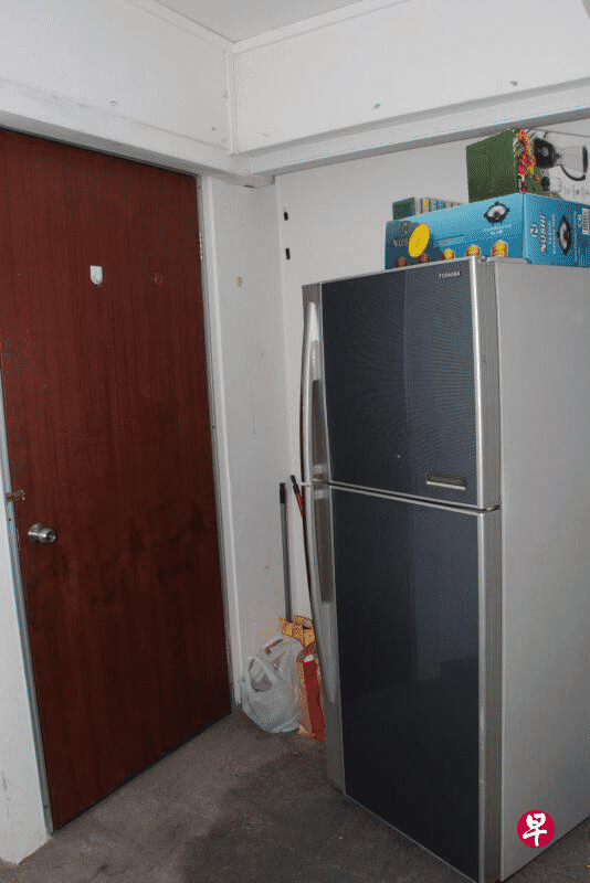 Refrigerator in a room with a wooden door and miscellaneous items on top.