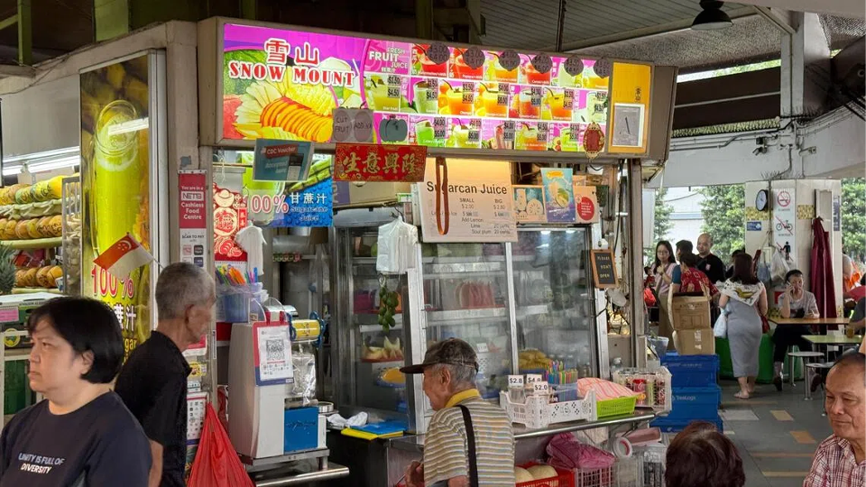 Snow Mountain fruit juice stand at a busy outdoor food market, vibrant and colorful, serving fresh beverages.
